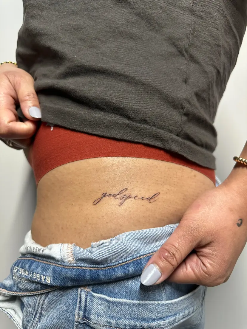 Script tattoo reading godspeed on the lower back