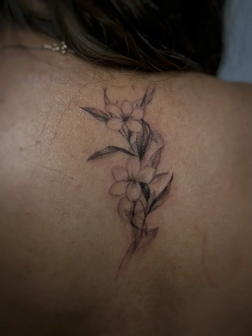 Fine-line flower branch tattoo on the upper back