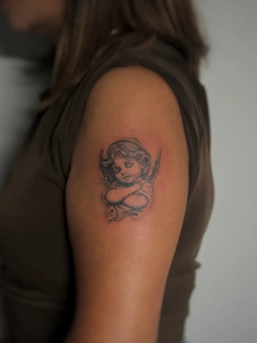 Black and grey cherub tattoo on an upper arm