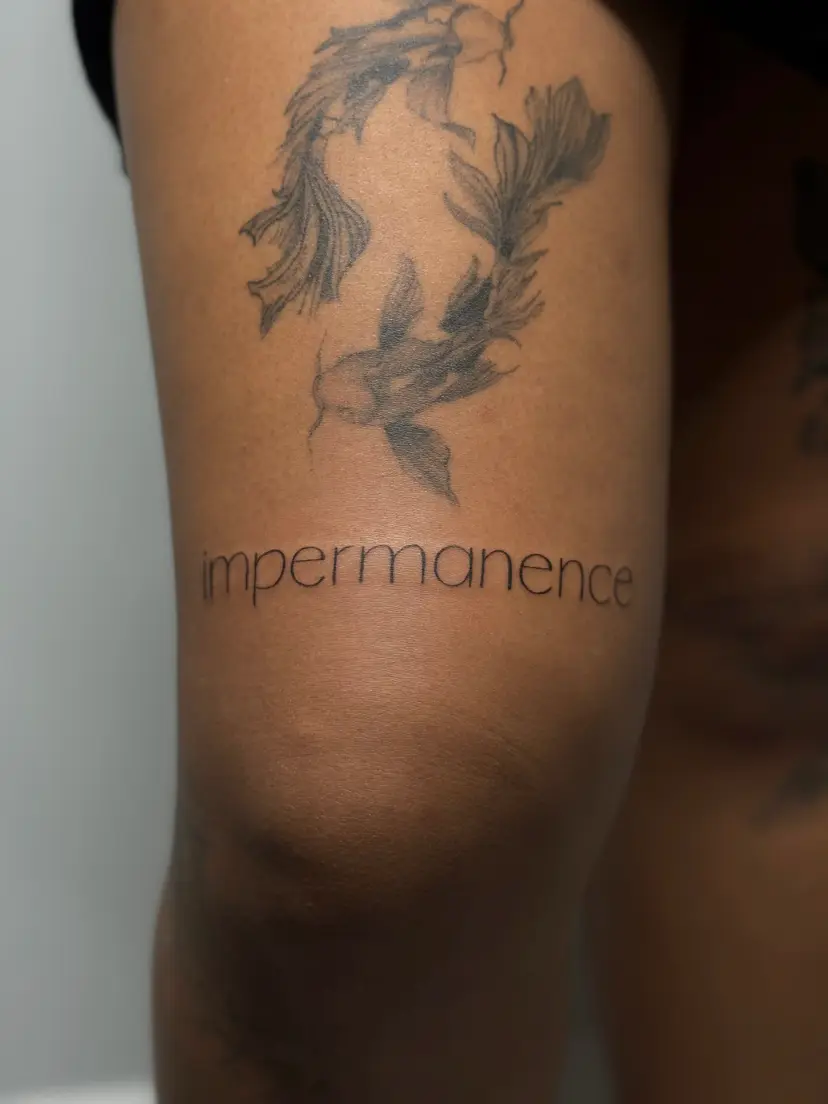 Two koi fish and the word impermanence tattooed on an arm