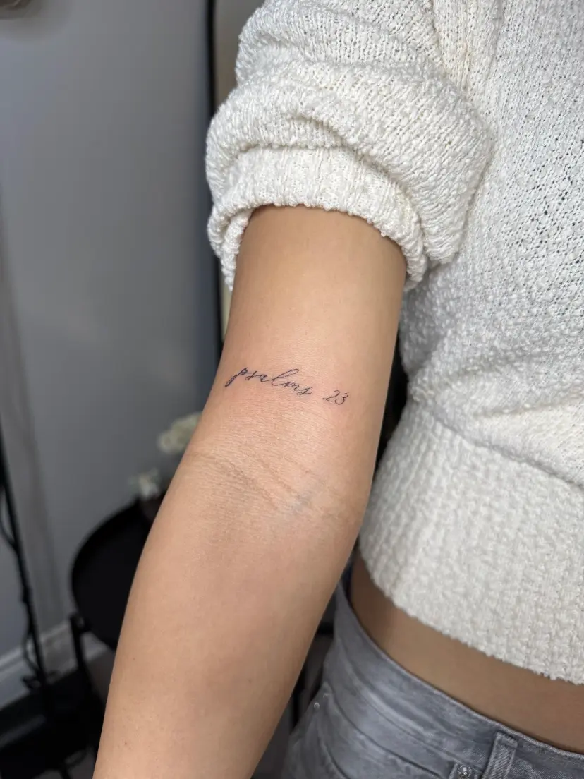Fine script tattoo reading psalms 23 on an inner arm