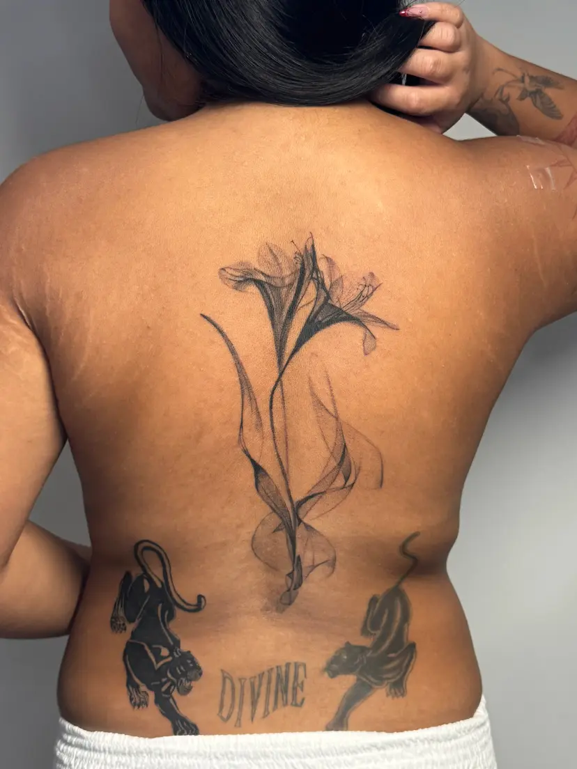 Black and grey lily and smoke tattoo down the spine
