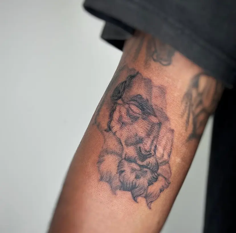 Black and grey tattoo of a face in prayer on an arm